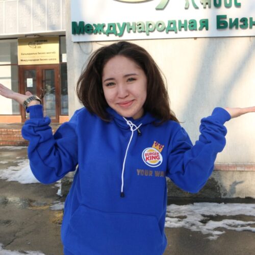 BAM Agency A person in a blue Burger King hoodie stands outside on the snowy ground, shrugging their arms. The scene unfolds before a building adorned with a sign in Russian, creating an intriguing blend of cultures. BAM Agency