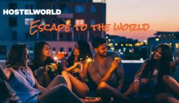 BAM Agency A group of five young people sits on a rooftop at night, holding sparklers and laughing. The city lights are blurred in the background. HOSTELWORLD Escape to the World is visible in the upper left corner, perfectly capturing the essence of todays vibrant youth market. BAM Agency