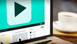 BAM Agency A person using a laptop displaying a sleek video player interface on the screen. A coffee cup rests on the wooden table beside it. The screen, with its large play button, hints at the future of social media engagement through immersive videos. BAM Agency