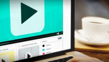 BAM Agency A person using a laptop displaying a sleek video player interface on the screen. A coffee cup rests on the wooden table beside it. The screen, with its large play button, hints at the future of social media engagement through immersive videos. BAM Agency