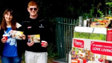 BAM Agency A group of five people stand outdoors, smiling and holding flyers and cups as part of a vibrant youth marketing campaign. There is a cart with pamphlets and a Fresh Student Living sign. Trees and a fence provide a pleasant backdrop. BAM Agency