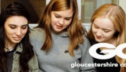 BAM Agency A group of five young adults, three females and two males, gather closely, smiling and looking at something off-image. Casually dressed, they exude excitement as they attend a Gloucestershire College brand open event. The college logo is visible on the bottom right. BAM Agency