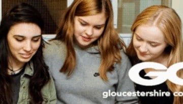 BAM Agency A group of five young adults, three females and two males, gather closely, smiling and looking at something off-image. Casually dressed, they exude excitement as they attend a Gloucestershire College brand open event. The college logo is visible on the bottom right. BAM Agency
