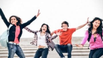 BAM Agency A group of eight freshers joyfully jump in the air with arms raised. They are on stairs, dressed in casual attire, and smiling. The background is a soft, overcast sky, capturing the youthful exuberance of student life. BAM Agency