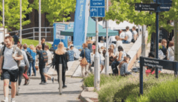 BAM Agency A lively outdoor scene unfolds at a university campus with students strolling past Exeter Guild of Students signs and food stands. Groups chat and relish the sunny day under green trees, embodying the vibrant essence of campus life. BAM Agency