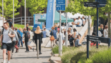 BAM Agency A lively outdoor scene unfolds at a university campus with students strolling past Exeter Guild of Students signs and food stands. Groups chat and relish the sunny day under green trees, embodying the vibrant essence of campus life. BAM Agency