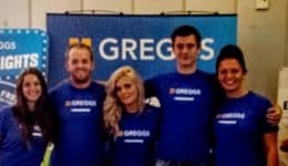 BAM Agency A group of six people wearing blue Greggs shirts stands in front of Greggs-themed posters and a spinning wheel display, smiling for the picture. It appears to be a lively Freshers event indoors, possibly managed by an enthusiastic Event Manager. BAM Agency