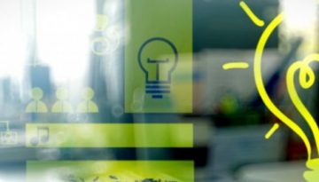 BAM Agency A blurred office setting showcases transparent diagrams and icons, including a flowchart, human figures, and a large bright yellow light bulb symbolizing creativity within a corporate brand. A hand is partially visible near the bulb, evoking a sense of innovation and ideas. BAM Agency