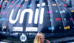 BAM Agency A large black inflatable structure with unii printed in vibrant colors stands impressively in an open indoor space. Crowd gathers, chatting excitedly about the student platforms launch, while signs for the App Store and Mobile Site adorn the eye-catching installation. BAM Agency