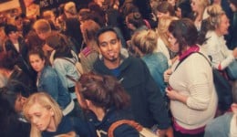 BAM Agency A crowded scene with people of various ages and ethnicities closely packed together at a vibrant UK student shopping event. Many engage in conversation or look around, the atmosphere lively with dim, warm lighting, suggesting a bustling BAM social gathering. BAM Agency