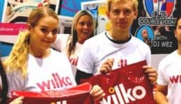 BAM Agency Four people wearing white Wilko t-shirts smile at the camera, holding Wilko bags. A large Wilko logo is visible in the background, capturing a vibrant moment of University Freshers engaged in dynamic youth marketing. BAM Agency