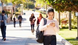 BAM Agency A woman strolls along a sunny campus path, eyes on her phone and a backpack slung over her shoulder. In the background, others are absorbed in their screens too. Surrounded by lush greenery and buildings, the scene buzzes with the latest insights from Students Unions. BAM Agency