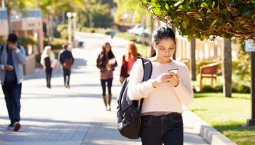 BAM Agency A woman strolls along a sunny campus path, eyes on her phone and a backpack slung over her shoulder. In the background, others are absorbed in their screens too. Surrounded by lush greenery and buildings, the scene buzzes with the latest insights from Students Unions. BAM Agency