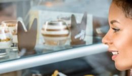 BAM Agency A woman with curly hair admires an assortment of desserts in a glass case. The layered parfaits and chocolate decorations, crafted by small brands, are arranged neatly across the shelves, perfect for capturing the attention of students passing by. BAM Agency