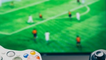 BAM Agency Two millennials engrossed in a soccer video game, gripping a white and a black controller, with the TV screen in the background showcasing their intense rivalry—a true testament to this generation of gamers. BAM Agency