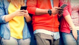 BAM Agency A group of students leans casually against a wall, each engrossed in their smartphone. Dressed in colorful tops and jeans, their faces are hidden as the focus is on how they interact with technology, offering a glimpse into understanding students today. BAM Agency
