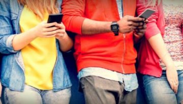 BAM Agency A group of students leans casually against a wall, each engrossed in their smartphone. Dressed in colorful tops and jeans, their faces are hidden as the focus is on how they interact with technology, offering a glimpse into understanding students today. BAM Agency