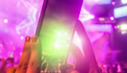 BAM Agency A smartphone held up in a colorful, crowded concert setting captures vibrant lights and stage effects. The scene buzzes with energy, featuring purple, pink, and green hues. Embracing trends from 2019, the blurred lights add a touch of nostalgia to the electric atmosphere. BAM Agency