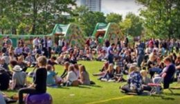 BAM Agency A large crowd of people sits on the grass at an outdoor event, featuring inflatable structures in the background. Trees and a few buildings dot the scene. Logos for BAM and Portsmouth Students Union add to the vibrant atmosphere, ensuring a lively community spirit. BAM Agency
