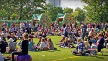 BAM Agency A large crowd of people sits on the grass at an outdoor event, featuring inflatable structures in the background. Trees and a few buildings dot the scene. Logos for BAM and Portsmouth Students Union add to the vibrant atmosphere, ensuring a lively community spirit. BAM Agency