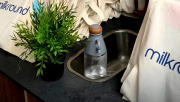 BAM Agency A countertop displays multiple canvas bags with the milkround logo, featuring a stylized milk bottle, as if ready for a university tour. Nearby, a small green plant and a transparent bottle with a wooden cap sit peacefully next to the sink. BAM Agency