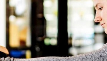 BAM Agency A person with long hair in a ponytail wearing a gray top browses through clothes on hangers, focusing intently on the latest fashion trends for todays youth. BAM Agency