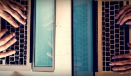 BAM Agency Two people typing on laptops facing each other across a white table. Their hands dance over the keyboards, perhaps crafting content for an influential student blogger. A smartphone rests between their laptops, and the warm lighting creates an inviting ambiance. BAM Agency