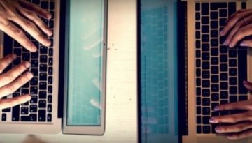 BAM Agency Two people typing on laptops facing each other across a white table. Their hands dance over the keyboards, perhaps crafting content for an influential student blogger. A smartphone rests between their laptops, and the warm lighting creates an inviting ambiance. BAM Agency