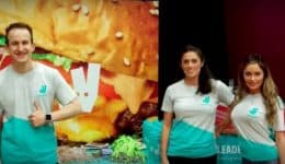 BAM Agency Four university students in Deliveroo t-shirts stand smiling in front of branded banners. The backdrop features a large, colorful image of a burger alongside the vibrant Deliveroo logo, capturing the essence of youthful energy and excitement in todays market. BAM Agency