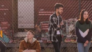 BAM Agency Five people are socializing by a chain-link fence with graffiti-covered train cars in the background. One person is sitting while the others stand, embodying a relaxed and upbeat vibe that speaks to the youthful energy important to todays brand-driven market. BAM Agency