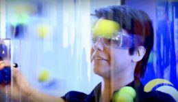 BAM Agency Amid a vibrant blur of colors, a person sporting safety goggles carefully drops yellow and blue balls into a clear vertical tube. This dynamic scene could easily be part of a captivating 2017 youth marketing strategy. BAM Agency