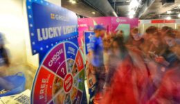 BAM Agency A bustling event scene unfolds with a Greggs Lucky Lights game wheel at its center, attracting a lively student market. The blurred motion captures the dynamic energy, while bright promotional signs and booths in the background encourage attendees to reconnect and engage safely. BAM Agency