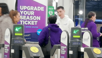 BAM Agency People walking through ticket barriers at a bustling transit station. Staff in purple jackets assist passengers as a Transpennine campaign encourages upgrading to a season ticket with a Smart Card. The scene is lively, filled with passengers and helpful staff. BAM Agency