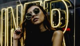 BAM Agency A woman in sunglasses stands in front of a reflective sign with the word DINER in large yellow neon letters. Sporting a sleeveless black top, she runs one hand through her hair, embodying the modern, urban vibe often seen in Instagram Influencer posts. BAM Agency