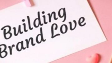 BAM Agency A white card displaying Building Brand Love rests against a pink background. Nearby, a heart-shaped pink stick adds charm, perfect for those aiming to build brand loyalty—even for the most unsexy brands. BAM Agency