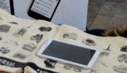 BAM Agency A table showcases canvas bags adorned with black illustrations, a tablet, and several branded items, featuring the WALL STREET JOURNAL logo. This display is part of a dynamic student marketing campaign. In the background, theres a poster with unreadable text. BAM Agency