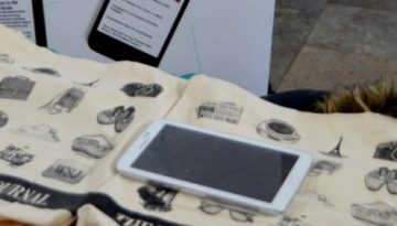 BAM Agency A table showcases canvas bags adorned with black illustrations, a tablet, and several branded items, featuring the WALL STREET JOURNAL logo. This display is part of a dynamic student marketing campaign. In the background, theres a poster with unreadable text. BAM Agency